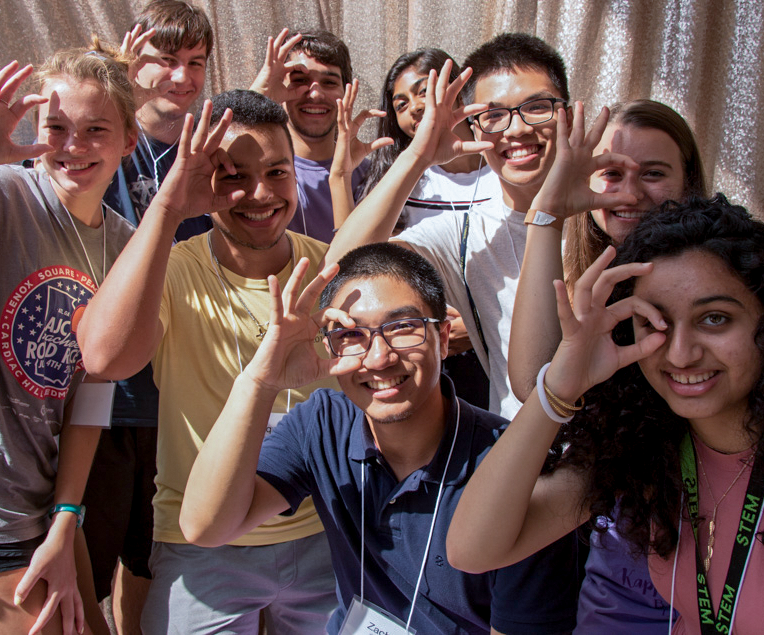 A groups of female and male students forming a C with their fingers.