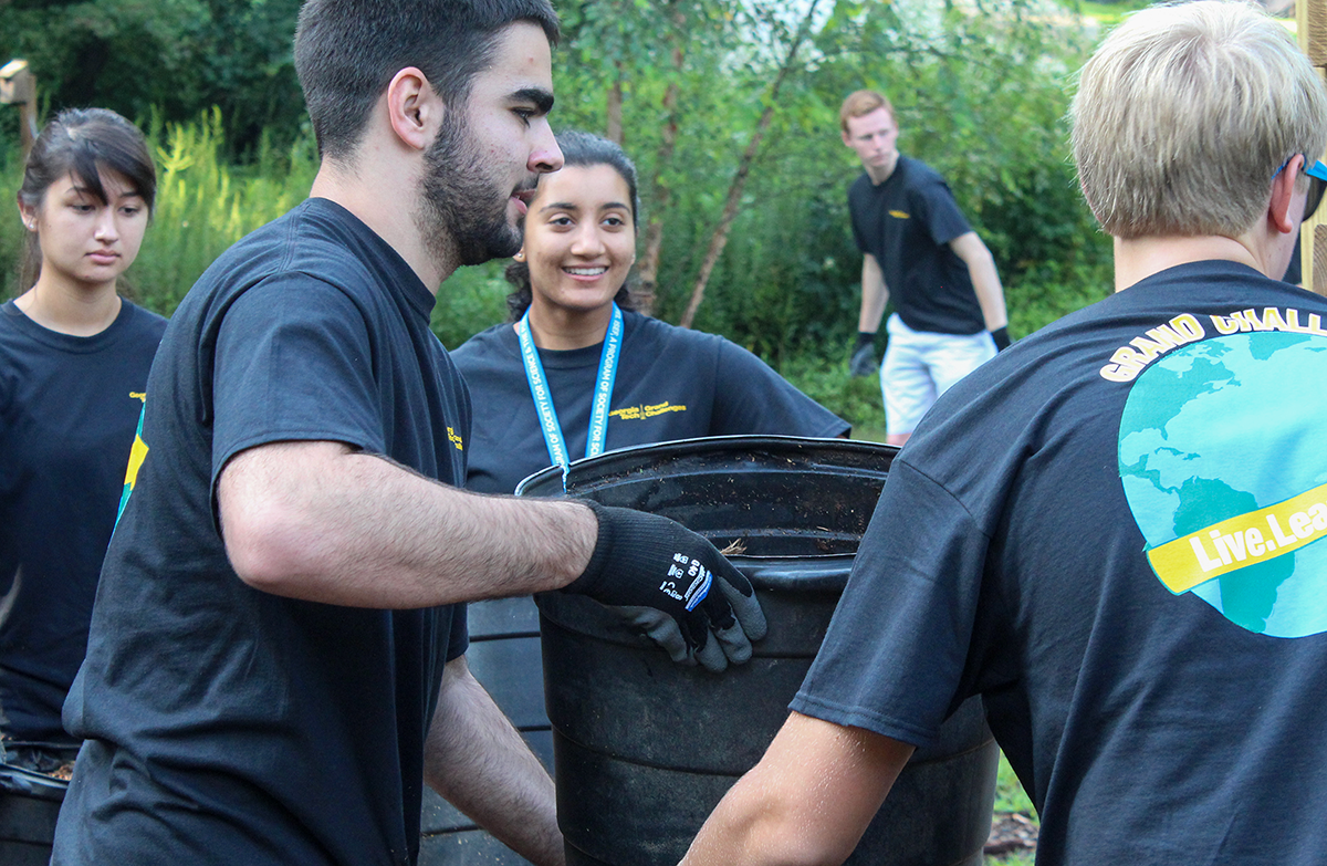 A group of students with a big black plastic bucket in a community garden.