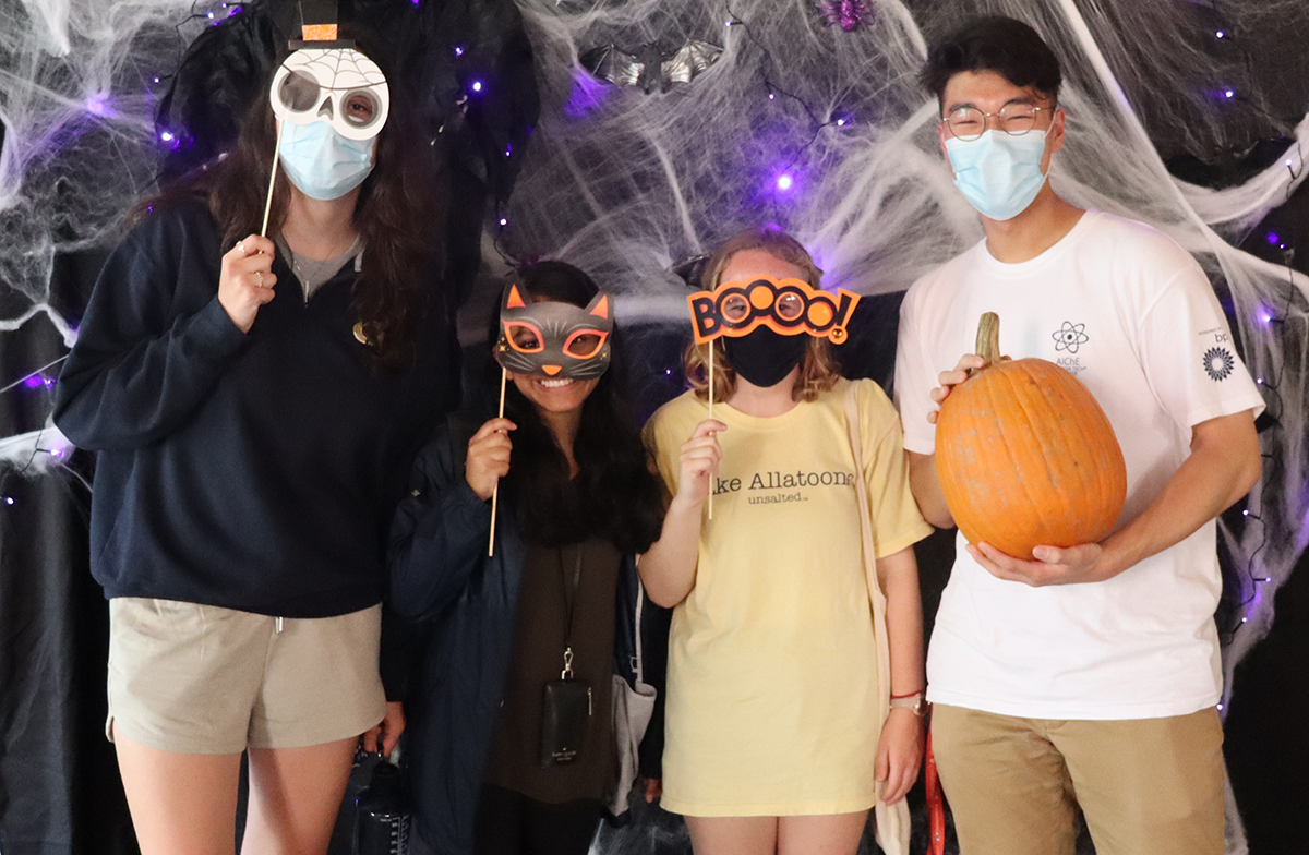 Three students using Halloween masks and one holding a pumpkin.