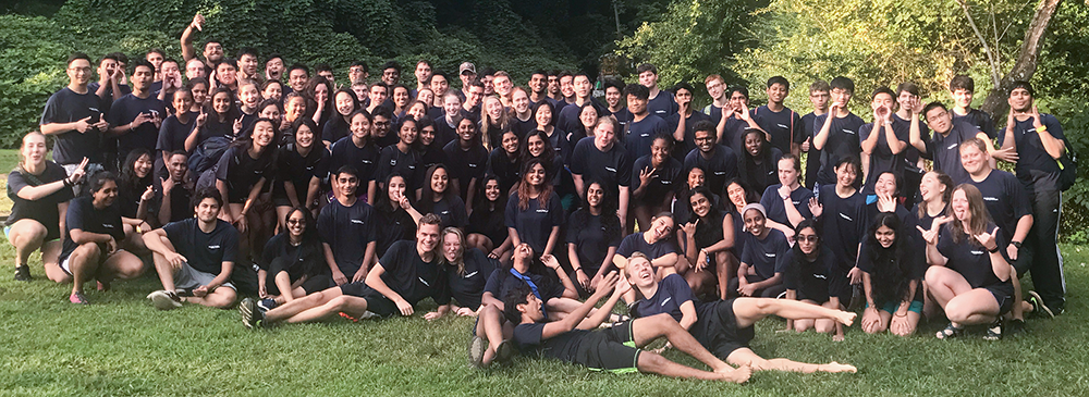 A large group of women and men students sitting on a green lawn. 