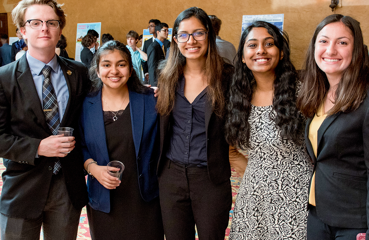 One man and four women students in business attire during a project presentation.