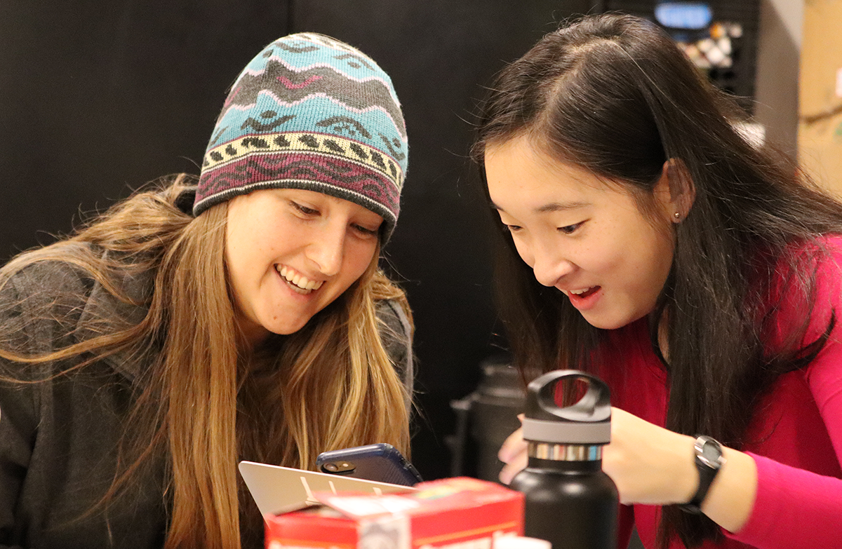 Two women students looking at a cellphone and smiling.