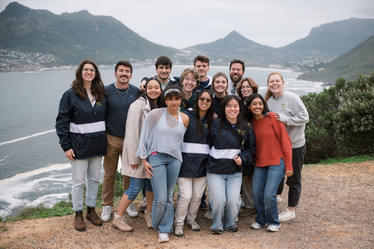 a group of college students stand together with a rocky shoreline behind them